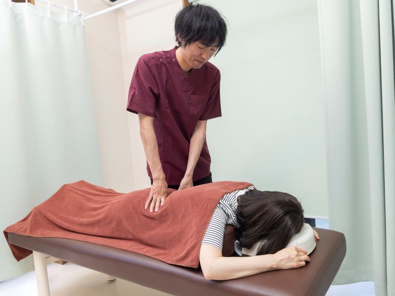 男性の背中をマッサージしている男性の手